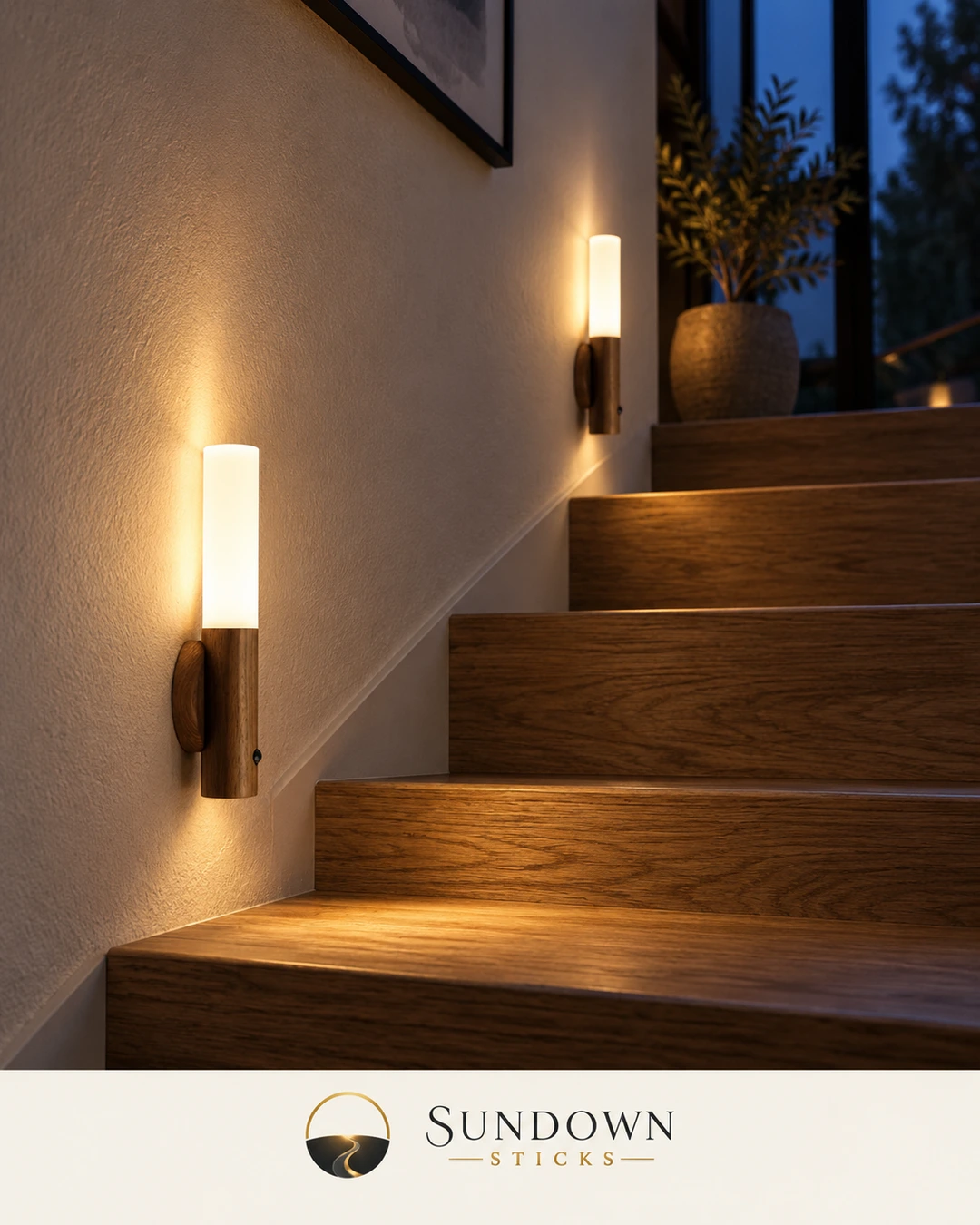 Two walnut-finish Sundown Sticks glowing warm white on the wall beside a wooden staircase at night